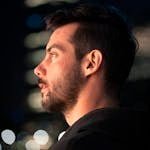 Portrait of a young man in a hoodie, gazing thoughtfully in a cityscape at night.